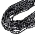 Sznury naturalnego, czarnego spinelu szliowanego na kształt drobnej kostki, ułożone w kiści na białym tle. Kamienie w rozmiarze 2,3x2,3mm