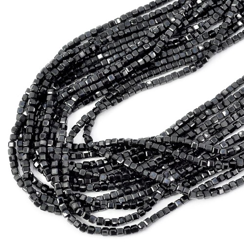 Sznury naturalnego, czarnego spinelu szliowanego na kształt drobnej kostki, ułożone w kiści na białym tle. Kamienie w rozmiarze 2,3x2,3mm