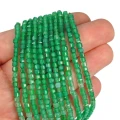 Drobne koraliki w kształcie fasetowanych kostek onyksu zielonego, w rozmiarze ok. 3x3mm. Nawleczone na zielone sznurki, prezentowane na dłoni, na białym tle.