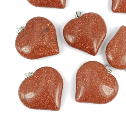 Zawieszki z piasku pustyni, w odcieniach miedzi z połyskującymi drobinkami, w kształcie dużego serca, z gotowym uchwytem do zawieszenia. Ujęcie z góry,  leżące luzem na białym tle.