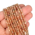 Kamienie w formie drobnych oponek fasetowanych w odcieniach beżu, koloru pomarańczowego i brązu, w rozmiarze ok. 3,5x2,8mm. Nawleczone na pomarańczowe sznurki. Prezentowane na dłoni, na białym tle.