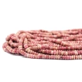 Kamienie w formie drobnych, nieregularnych oponek gładkich, w odcieniach różu, w rozmiarze ok. 2,5x4,5mm. Nawleczone na różowe sznurki. Widok z perspektywy bocznej, leżące w zwiniętej kiści na białym tle.