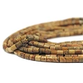 Kamienie w formie gładkich walców z jaspisu obrazkowego, o wymiarach ok. 4 × 4,5 mm. Nawleczone na żółte sznurki.  Widok z perspektywy bocznej – leżą w zwiniętej kiści na białym tle.