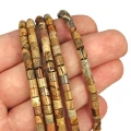 Kamienie w formie gładkich walców z jaspisu obrazkowego, o wymiarach ok. 4 × 4,5 mm. Nawleczone na żółte sznurki.  Prezentowane na dłoni na białym tle.