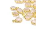 Okrągłe, zawieszki fasetowane z naturalnym kwarcem różowym ok.10x7 mm, oprawione w srebro pozłacane 925, idealne do naszyjników i bransoletek, widok z perspektywy bocznej, leżące luzem na białym tle