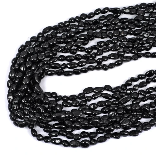 Kamienie w formie nieregularnych gładkich bryłek czarnego turmalinu, w rozmiarze ok. 5-10x4-6mm. Nawleczone na czarne sznurki. Ujęcie z góry, leżące w zwiniętej kiści na białym tle.