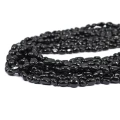 Kamienie w formie nieregularnych gładkich bryłek czarnego turmalinu, w rozmiarze ok. 5-10x4-6mm. Nawleczone na czarne sznurki. Widok z perspektywy bocznej, leżące w zwiniętej kiści na białym tle.